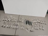 Full assortment of Roger Bros cutlery laid out on a table, showing spoons, forks, knives, and serving pieces in 1847 pattern stainless steel.