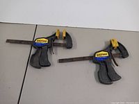 Photo showing two Quick-Grip bar clamps with yellow pads, black handles, and blue brand labels. Metal bars have visible rust.
