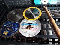 Five used circular saw blades arranged on a crate surface showing brand names and blade teeth.