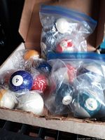 Box with multiple Sears pool cue balls in plastic bags, showing some balls split and cracked.