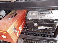 Photo showing both tool boxes on a black metal shelf, the red Craftsman metal toolbox with handle and metal clasps on the left and the black Husky plastic toolbox with a transparent top on the right.