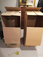Two U-Haul travel closet boxes side by side, open top and front flaps visible, standing upright on carpeted floor with measuring tape in front for scale.