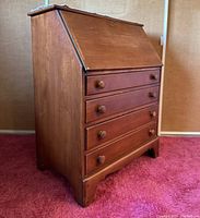Side angle view of antique maple drop front secretary desk showing wood grain, drawer knobs, and bracket feet.