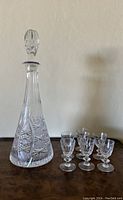 Full view of the vintage Bohemian conical etched crystal decanter with six matching stemmed glasses arranged beside it on a wooden surface.