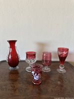 Five red art glass pieces arranged on a wooden surface against a plain wall