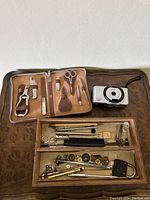 Photo showing open manicure kit case, film camera, and wooden box of jewelry tools