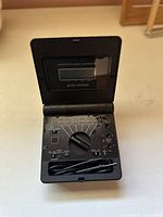 Front view of the Micronta folding multimeter open showing the measurement dial, display, and included test leads.