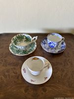 Photo showing all three teacups and saucers arranged on a wooden table, featuring green, blue, and white color designs.