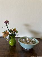 Photo showing the green vase with multiple colorful seed bead flower brooches next to a light blue bowl with white flower brooches