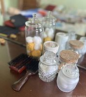 Photo showing vintage brushes and various glass jars on a table, some jars filled with cotton balls and pills