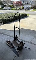 Full view of metal dolly hand truck and two vintage saws on concrete driveway.