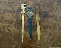 Three vintage metal letter openers laying flat on a wood surface, showing the horse head design, Israel emblem, and brass finish.