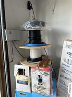 Photo of stacked wiring spools with black, blue, and white cables on wooden reels, with some boxes underneath.