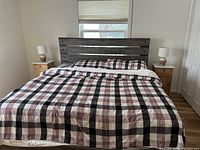 Front view of king size bed frame with slatted headboard, mattress with plaid comforter, pillows, nightstands and lamps