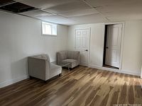 Photo of two beige upholstered side chairs positioned against a white wall in a room with wood tone floor and white doors.