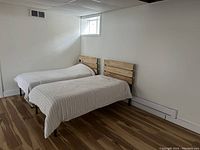 Photo of two single beds with wood slat headboards in a minimally furnished room showing bedding and one headboard with one screw missing as noted by the seller.