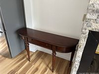 Wood console table against a wall showing its full length, drawer, and leg details.