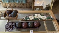 Top-down photo of eight bocce balls, wooden floral plaque, basket, and sun face wall art on glass coffee table