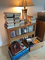 Photo of stacked books on a wooden book display case with more books stacked on the top and in boxes below.