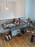 Long black folding catering table covered with assorted household items in a well-lit room.
