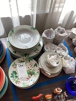Photo showing stacks of plates, bowls, cups and saucers with holiday holly and red berry pattern, white background with green rim.