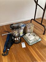 Lot items arranged on hardwood floor including camping lantern, umbrellas, Kidde fire alarm, wall clock, brass wall sconce, and Olde Brooklyn lantern box
