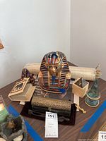 Wide view of lot items showing Tutankhamen bust center, mini pyramids, scrolls, decanter, books and small figurines on table.