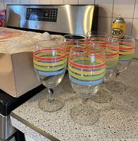 Set of six stemmed glasses with colorful stripes on a kitchen counter near stove