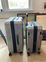 Two silver Olympia poly hard shell luggage pieces side by side showing size difference and handles.