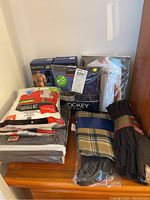 Photo showing packaged men's t-shirts by Nautica, Galaxy, and Hanes 3-pack tagless white t-shirts, various socks by Gold Toe, a plaid scarf in beige/navy/gray, and boxed navy Jockey boxer briefs.