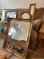 Photo showing multiple mirrors with ornate gold-tone frames arranged on a sofa. One large rectangular mirror is prominent in foreground.