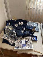 Photo of New York Yankees apparel and collectibles arranged on a table including jersey, t-shirt, slippers, bobblehead, and framed photo