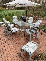 Full view of the entire outdoor patio set on a brick patio, showing six cushioned chairs, two stools, rectangular glass-top table, and umbrella.