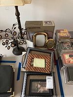 Photo showing a collection of assorted picture frames including a Pandigital digital photo frame in box, multiple frames in gold and black finishes, and a metal frame tree with several small hanging oval frames.