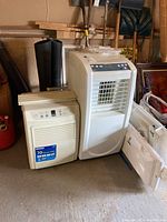 Kenmore 70 pint dehumidifier and SPT portable air conditioner side by side in garage space, showing overall condition and size.
