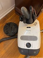 Top view of Miele Olympus canister vacuum cleaner with attached nozzle tools, sitting on wooden floor.