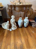 Pair of Franklin porcelain vases and two white cherub figurines displayed on the floor in front of a wooden table.