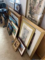 View of seven pieces of wall art leaning against wall, showing size and variety of frames and subjects including floral and architectural prints.