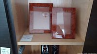 Two smaller Natalini birdseye wood picture frames, 5x7 and 4x6, on a shelf labeled lot 145.