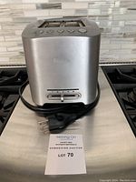 Front view of Breville 2-slice toaster showing brand logo, control buttons, cord and plug on stainless steel surface.