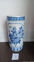 Full frontal view of the glazed cylindrical umbrella stand showing a large floral motif and decorative patterned band near the top and bottom edges.