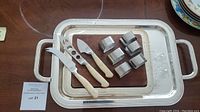 Set displaying large silver plated tray, wooden cheese board, 6 silver napkin rings, and three cheese tools with ivory handles