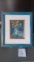Full view of framed oil painting showing flower bouquet in white pitcher with ceramic cup and apple, in teal wood and gold frame with beige mat.