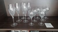 5 tall Stuart crystal champagne glasses and 6 rounded ice wine glasses arranged on a shelf.