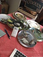Photo showing collection of animal-themed decorative plates arranged on a table including designs of cats, birds, ducks, pandas, and elephants.