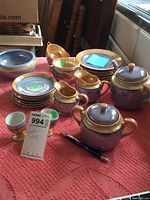 Full view of the collected lot showing all blue and gold lusterware plates, tea set pieces, and cups arranged on a red cloth table covering.