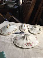 Set of four porcelain casserole lids on a table with pen for scale, showing various floral designs and shapes