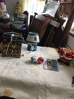 Photo showing Christmas themed items on white cloth including ornaments, light-up toy bin, headless Santa planter, tree platter, tea light holder, and Christmas cards.