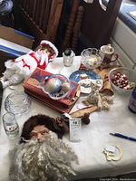 Overview of Christmas box items displayed on a table including dolls, glass ornaments, Santa head figurine, decorative plates, and small decorative holiday pieces.