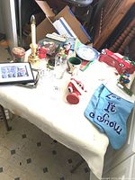 Wide view of the Christmas mashup items on a table including candles, glasses, Santa figure, plate, mitts, and framed art.